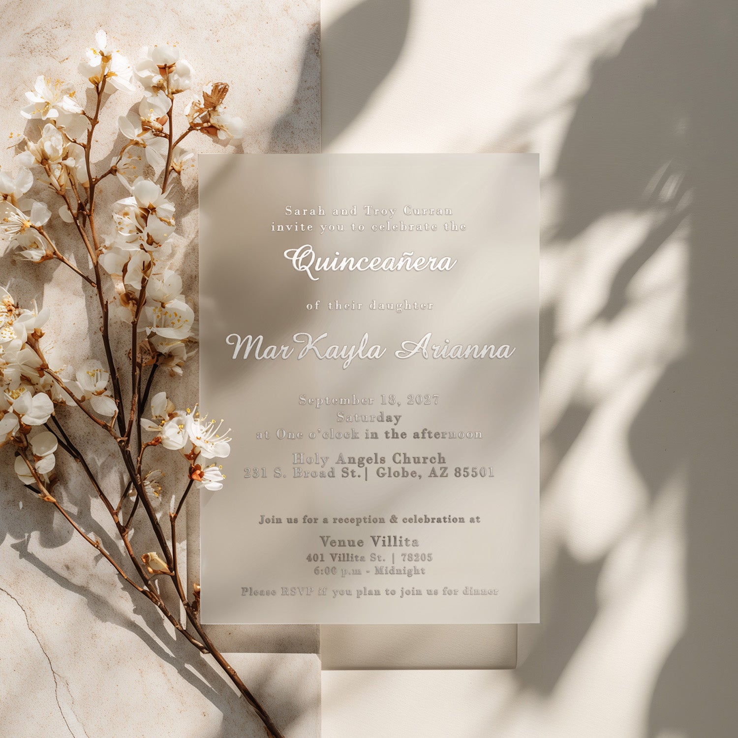 XOXOKristen translucent vellum quinceañera invitation with shimmering silver foil lettering placed beside delicate white cherry blossoms on a sunlit neutral stone surface. The soft natural lighting highlights the reflective foil and frosted transparency of the vellum paper, creating a dreamy and luxurious look for an elegant 15th birthday celebration - XOXOKristen