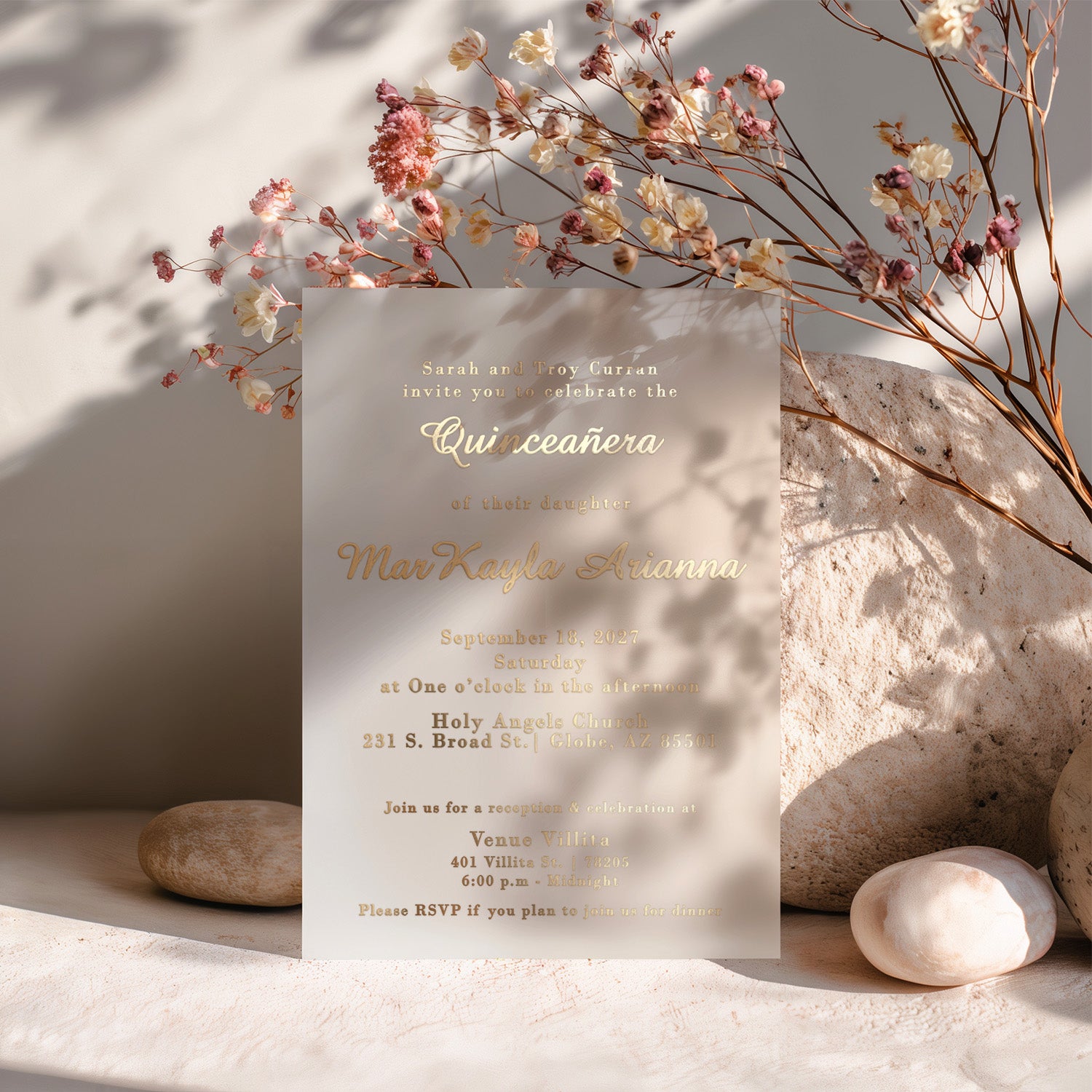 XOXOKristen personalized vellum quinceañera invitation standing upright among dried pastel florals and soft rocks, with sunlight casting gentle shadows. The metallic gold foil printing glows beautifully under natural light, enhancing the frosted translucence of the vellum card. Perfect for showcasing luxury quinceañera invitations designed for 15th birthday celebrations with elegance and warmth.