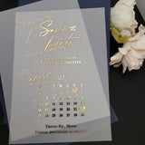 Luxurious vellum Save the Date card printed with gold foil lettering, standing upright among neutral stones and dried florals under soft light, highlighting its translucent texture and elegant minimalist design – XOXOKristen