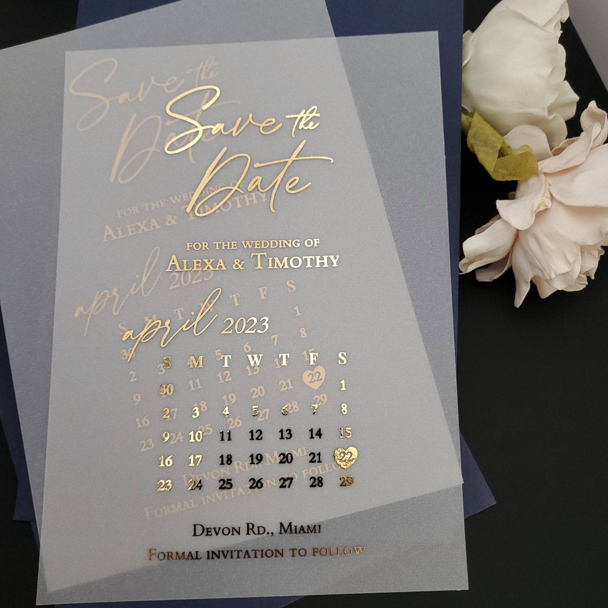 Luxurious vellum Save the Date card printed with gold foil lettering, standing upright among neutral stones and dried florals under soft light, highlighting its translucent texture and elegant minimalist design – XOXOKristen