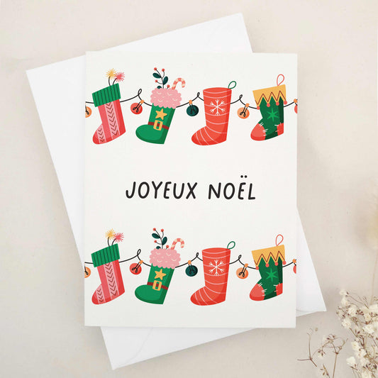 Charming 'Joyeux Noël' card that immerses you in French holiday tradition, featuring a playful array of festive stockings, each uniquely adding a sprinkle of Christmas magic. The design embodies joy and whimsy of the festive season, with stockings showcasing different aspects of holiday cheer, blending traditional French elegance with a playful holiday spirit.