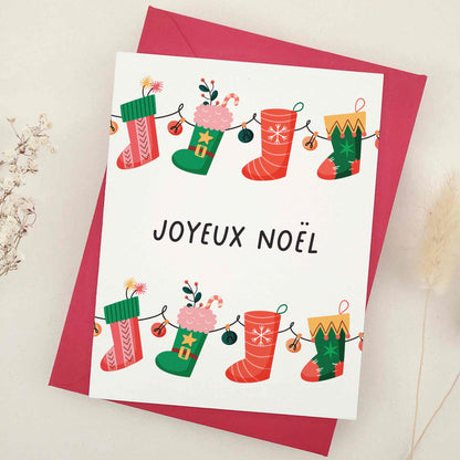 Charming 'Joyeux Noël' card that immerses you in French holiday tradition, featuring a playful array of festive stockings, each uniquely adding a sprinkle of Christmas magic. The design embodies joy and whimsy of the festive season, with stockings showcasing different aspects of holiday cheer, blending traditional French elegance with a playful holiday spirit.