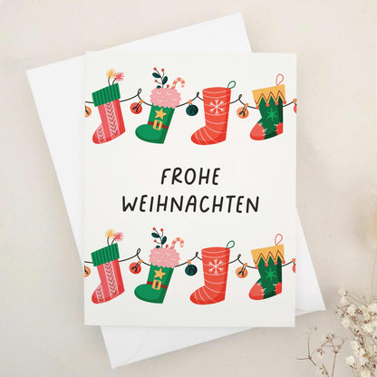 Delightful 'Frohe Weihnachten' card adorned with whimsical Christmas stockings, each festively decorated to capture the cozy and cheerful spirit of the season. The stockings, strung together like a garland, symbolize the connection and joy of the holidays. This card combines traditional German holiday charm with a touch of whimsy, making it perfect for sharing festive wishes.