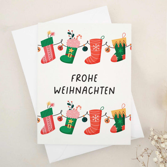 Delightful 'Frohe Weihnachten' card adorned with whimsical Christmas stockings, each festively decorated to capture the cozy and cheerful spirit of the season. The stockings, strung together like a garland, symbolize the connection and joy of the holidays. This card combines traditional German holiday charm with a touch of whimsy, making it perfect for sharing festive wishes.