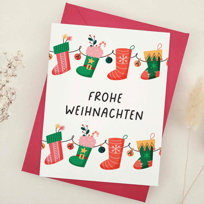 Delightful 'Frohe Weihnachten' card adorned with whimsical Christmas stockings, each festively decorated to capture the cozy and cheerful spirit of the season. The stockings, strung together like a garland, symbolize the connection and joy of the holidays. This card combines traditional German holiday charm with a touch of whimsy, making it perfect for sharing festive wishes.