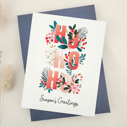 Spread holiday cheer with our beautifully crafted 'Ho Ho Ho' Season's Greetings card, featuring festive flowers, Christmas berries, and a playful 'Ho Ho Ho' typographic arrangement, a heartfelt way to celebrate the season.