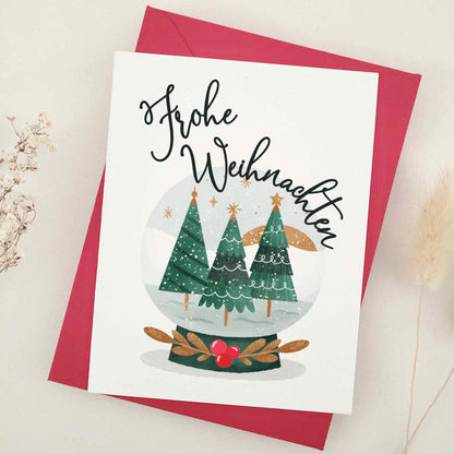 Heartfelt 'Frohe Weihnachten' card, featuring an idyllic snow globe scene with stately evergreens, evoking the tranquil beauty of a traditional German Christmas. This picturesque representation of the serenity and majesty of winter is ideal for conveying warm season's greetings with a touch of German tradition.