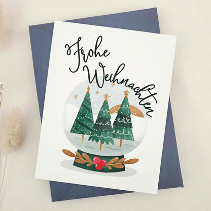 Heartfelt 'Frohe Weihnachten' card, featuring an idyllic snow globe scene with stately evergreens, evoking the tranquil beauty of a traditional German Christmas. This picturesque representation of the serenity and majesty of winter is ideal for conveying warm season's greetings with a touch of German tradition.