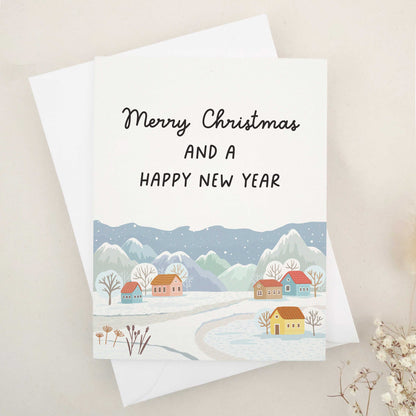 Picturesque 'Merry Christmas and a Happy New Year' card, featuring a tranquil village scene with snow-capped mountains in the background. This beautifully crafted card harmoniously blends nature's grandeur and quaint village charm, symbolizing peace and hope of the festive season. It artistically represents the serene beauty of winter and the joyful anticipation of a new year.