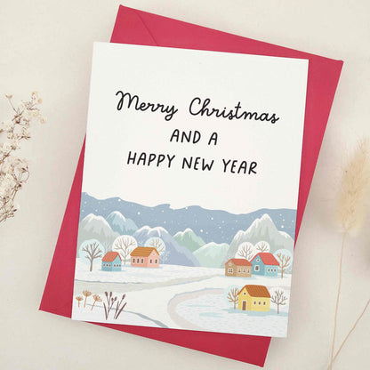 Picturesque 'Merry Christmas and a Happy New Year' card, featuring a tranquil village scene with snow-capped mountains in the background. This beautifully crafted card harmoniously blends nature's grandeur and quaint village charm, symbolizing peace and hope of the festive season. It artistically represents the serene beauty of winter and the joyful anticipation of a new year.