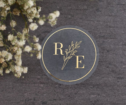 Clear custom wedding sticker with golden initials and botanical illustration.