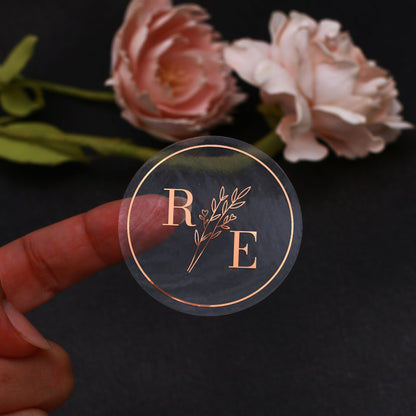 Clear custom wedding sticker with golden initials and botanical illustration.