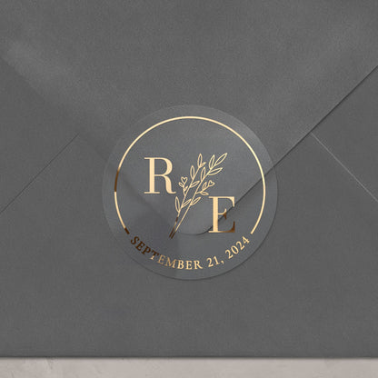 Transparent wedding sticker with golden initials and date, featuring an elegant botanical design