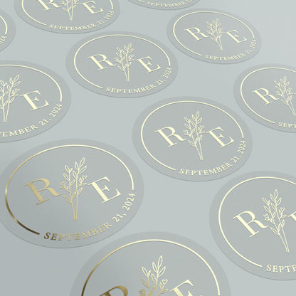 Transparent wedding sticker with golden initials and date, featuring an elegant botanical design