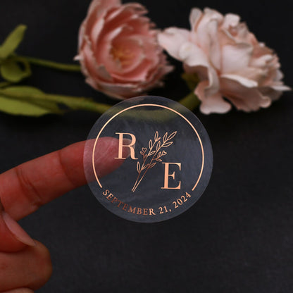 Transparent wedding sticker with golden initials and date, featuring an elegant botanical design
