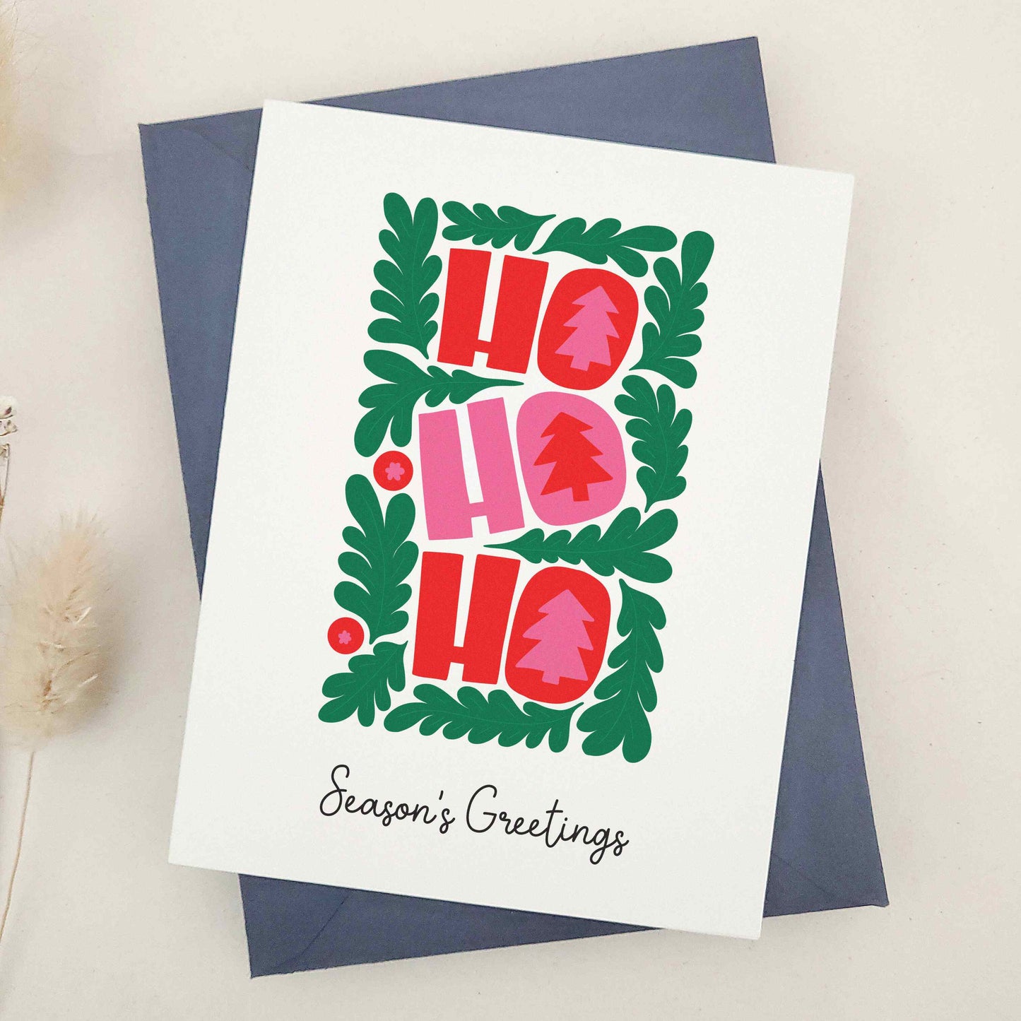Spread holiday cheer with our vibrant 'HO HO HO' Season's Greetings card, featuring a festive wreath and bold Christmas trees, a delightful and eye-catching way to brighten the holiday season for friends and family.