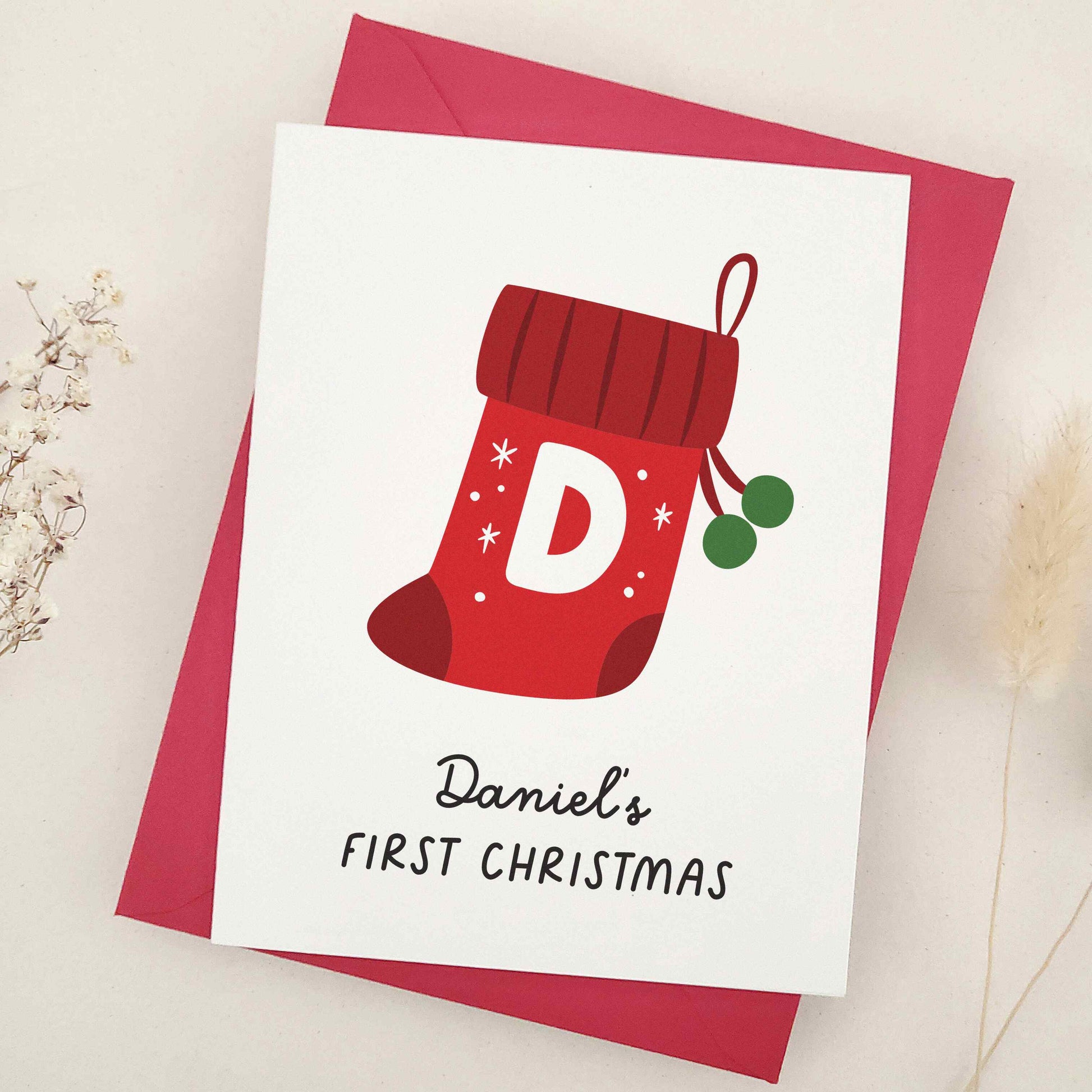 Daniel's First Christmas card: capture the magic of a memorable milestone with a sweet keepsake featuring a cheerful red stocking, bold initial, and festive snowflakes, celebrating a child's first holiday season.
