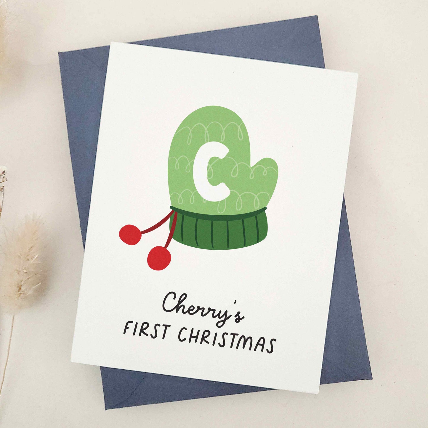 Share the happiness and joy of the season with a heartwarming design featuring a cozy green winter mitten adorned with a playful initial, perfect for marking a little one's introduction to time-honored holiday traditions. This delightful card captures the essence of a child's first experience with the magic of yuletide, making it a cherished keepsake for years to come.
