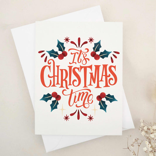 Elegant 'It's Christmas Time' card, lavishly expressing holiday excitement and joy, adorned with traditional holly leaves and berries. Features a beautifully styled typographic design as the centerpiece, joyously announcing the season and capturing the essence of holiday merriment. This card combines classic holiday imagery with modern typographic flair, making it a sophisticated and festive choice for season's greetings.