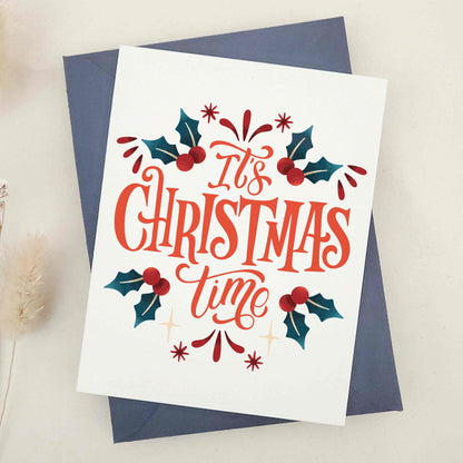 Elegant 'It's Christmas Time' card, lavishly expressing holiday excitement and joy, adorned with traditional holly leaves and berries. Features a beautifully styled typographic design as the centerpiece, joyously announcing the season and capturing the essence of holiday merriment. This card combines classic holiday imagery with modern typographic flair, making it a sophisticated and festive choice for season's greetings.