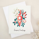 Folded holiday card featuring the word “JOY” in coral red letters surrounded by soft cream leaves, berries, and foliage, with “Season’s Greetings” below — XOXOKristen.