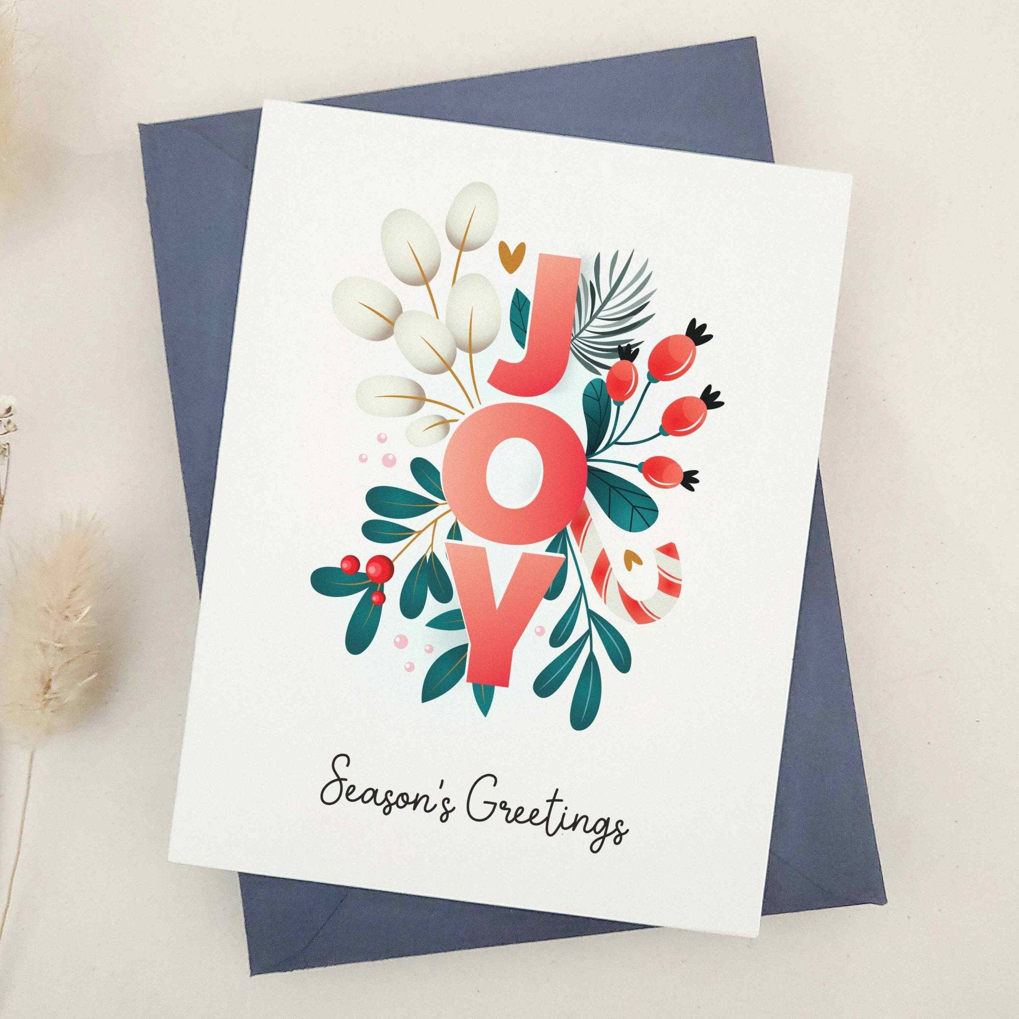 Standing card with “JOY” floral design and “Season’s Greetings” text, displayed with a coordinating envelope — XOXOKristen.