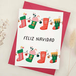 Standing card with playful stocking garland design, vibrant reds and greens, and “Feliz Navidad” message, styled with red envelope — XOXOKristen.