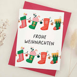 Standing card with festive stocking garland design in red and green, with “Frohe Weihnachten” greeting, styled with red envelope — XOXOKristen.