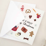 Standing card with “Have a Holly Jolly Christmas” greeting surrounded by holiday treats and gifts, styled with white envelope — XOXOKristen.