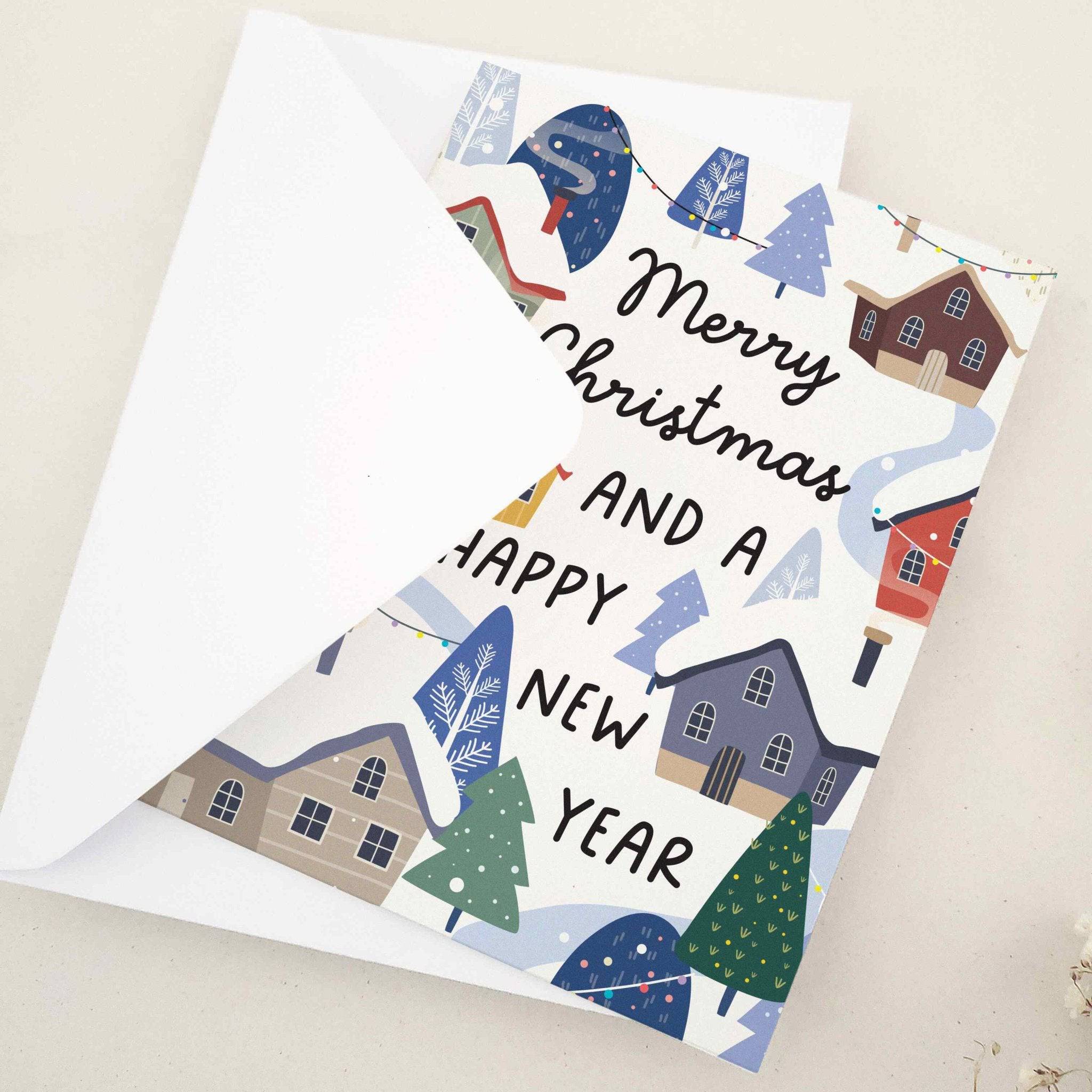 Folded holiday card featuring cozy pastel houses, snow-covered roofs, frosted pine trees, and winding snowy paths beneath the greeting, displayed with envelope — XOXOKristen.