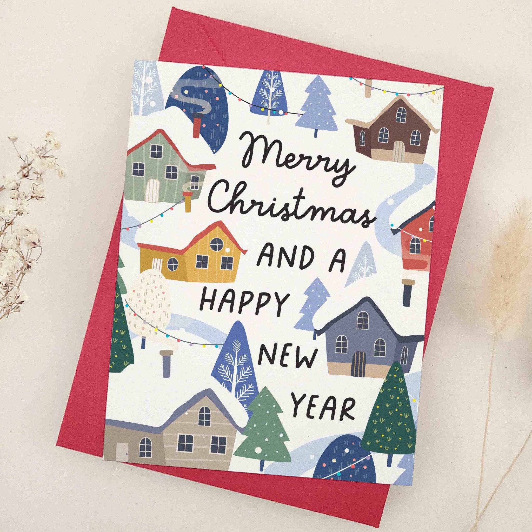 Holiday card decorated with multi-colored cottages, frosty hills, and evergreen trees beneath festive holiday greeting, styled with red envelope — XOXOKristen.