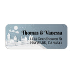 Close-up of winter village return address label with white cut-out style buildings, snowflakes, and bold printed text - XOXOKristen