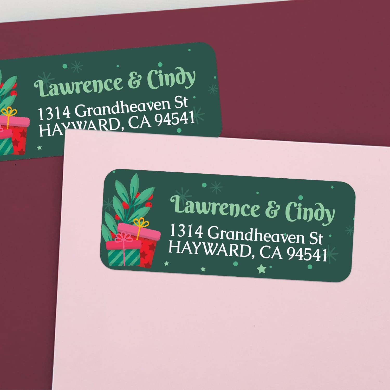 Personalized holiday address labels on pink and burgundy envelopes with festive gift box illustrations and green background – XOXOKristen