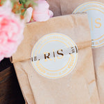 XOXOKristen clear round wedding favor stickers with metallic foil, sealing brown kraft paper bags for rustic and elegant wedding gift packaging.