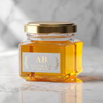 Glass jar with gold lid decorated with rectangular wedding label, serif initials framed by metallic foil foliage accents – XOXOKristen.