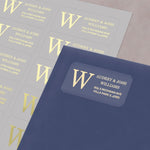 XOXOKristen gold foil monogram address label with bold initial and personalized names, printed on clear PVC vinyl, applied to navy blue envelope - XOXOKristen