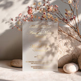 vellum wedding invitation printed in luxurious gold foil lettering, standing upright among soft dried flowers and warm light, highlighting its delicate transparency and elegant typography – XOXOKristen