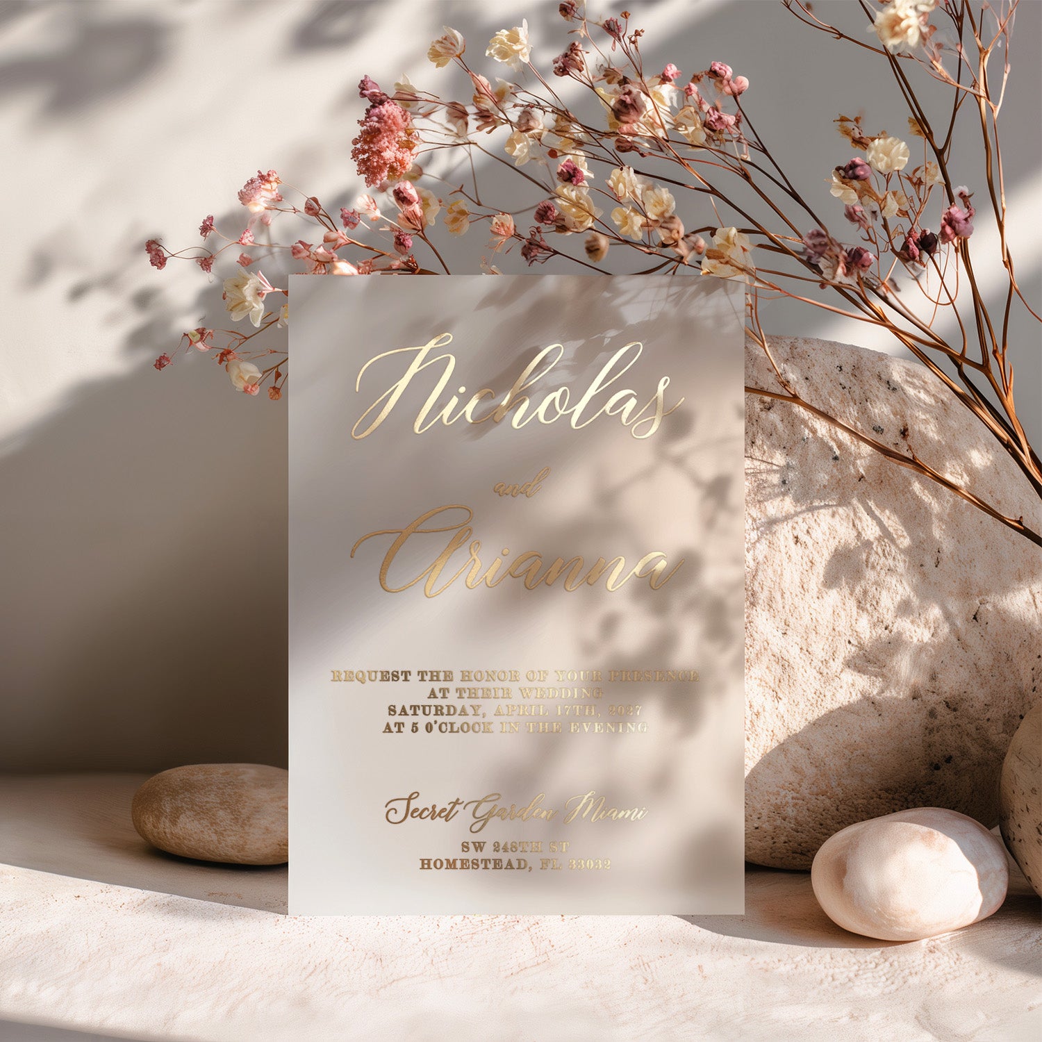 Elegant vellum invitation card with gold foil printing displayed on soft stone background with pastel flowers and subtle shadows. Perfect for modern or luxury wedding announcements. - XOXOKristen