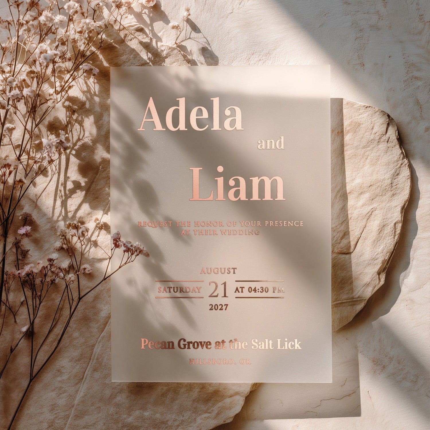 A translucent vellum wedding invitation printed in elegant rose gold foil, displayed on neutral tones with dried floral accents. The shimmering foil reflects the sunlight beautifully, emphasizing the romantic and delicate nature of this wedding stationery – XOXOKristen.