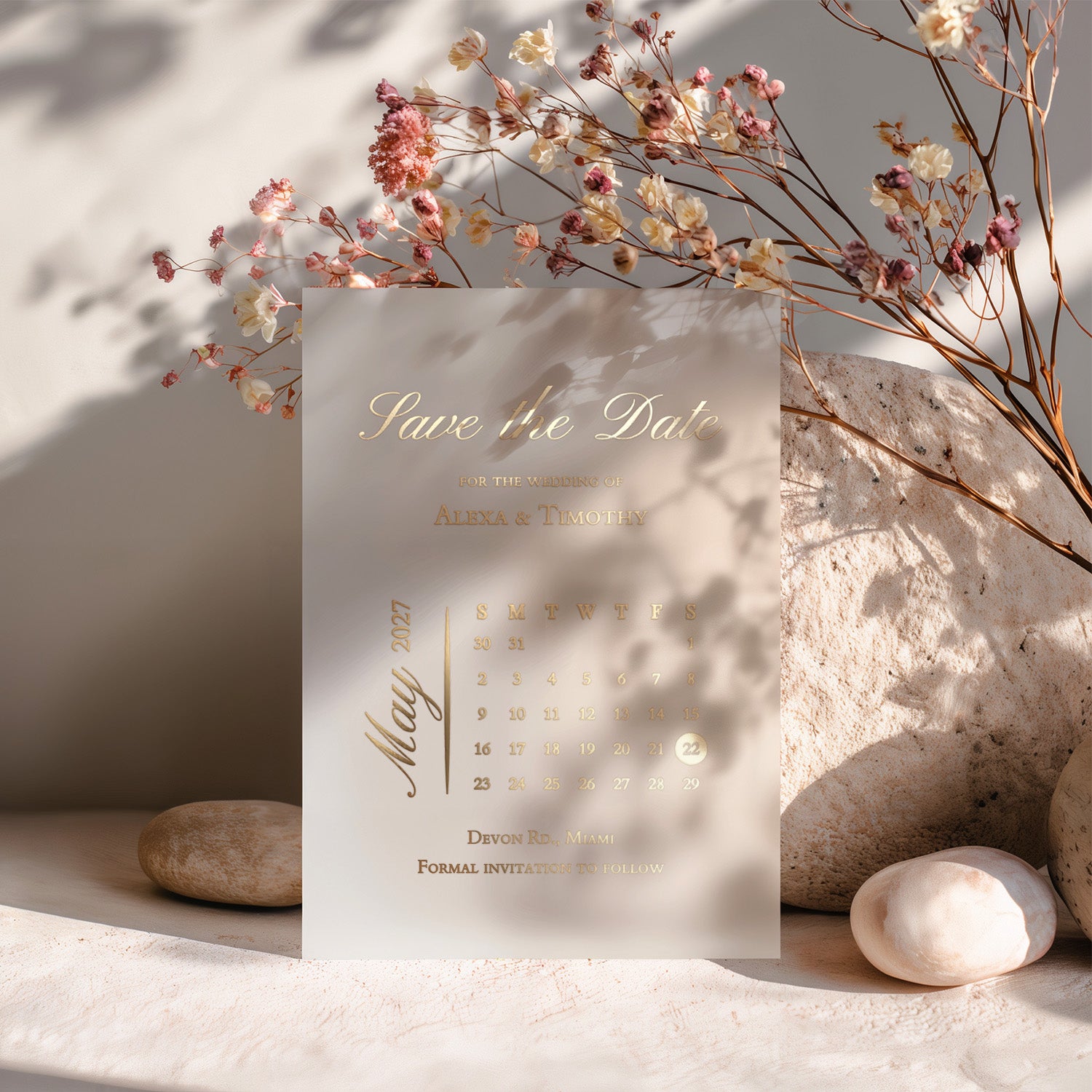Gold-foiled acrylic “Save the Date” card placed among dried florals and soft stone textures, perfect for luxury minimalist weddings – XOXOKristen