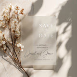 XOXOKristen vellum Save the Date card featuring reflective silver foil text and elegant script lettering, styled with white spring blossoms on a neutral surface for a soft romantic look – XOXOKristen.