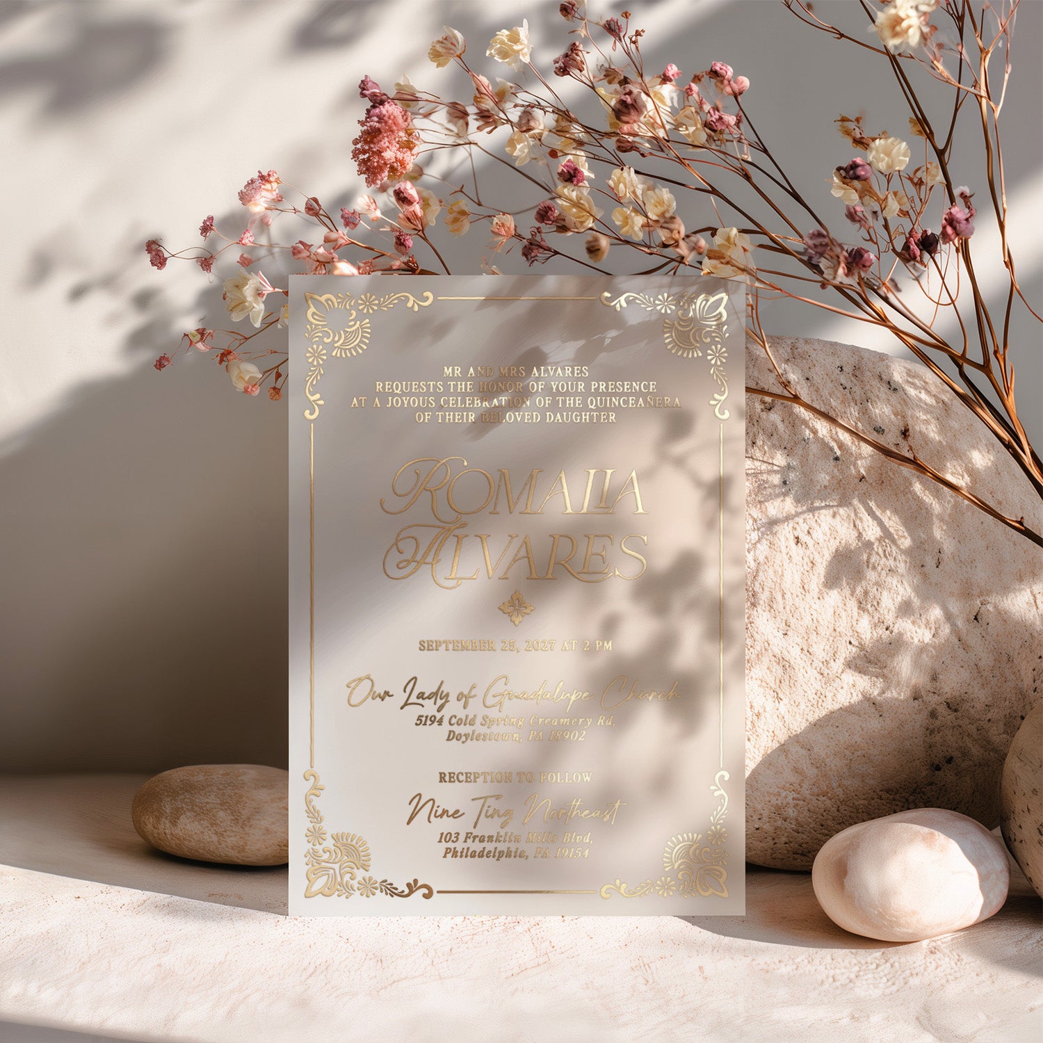 Vellum quinceañera invitation printed in metallic gold foil lettering, standing upright among dried florals and neutral stones, highlighting its translucent texture, ornate detailing, and luminous finish – XOXOKristen