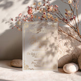 Vellum quinceañera invitation printed in metallic gold foil lettering, standing upright among dried florals and neutral stones, highlighting its translucent texture, ornate detailing, and luminous finish – XOXOKristen