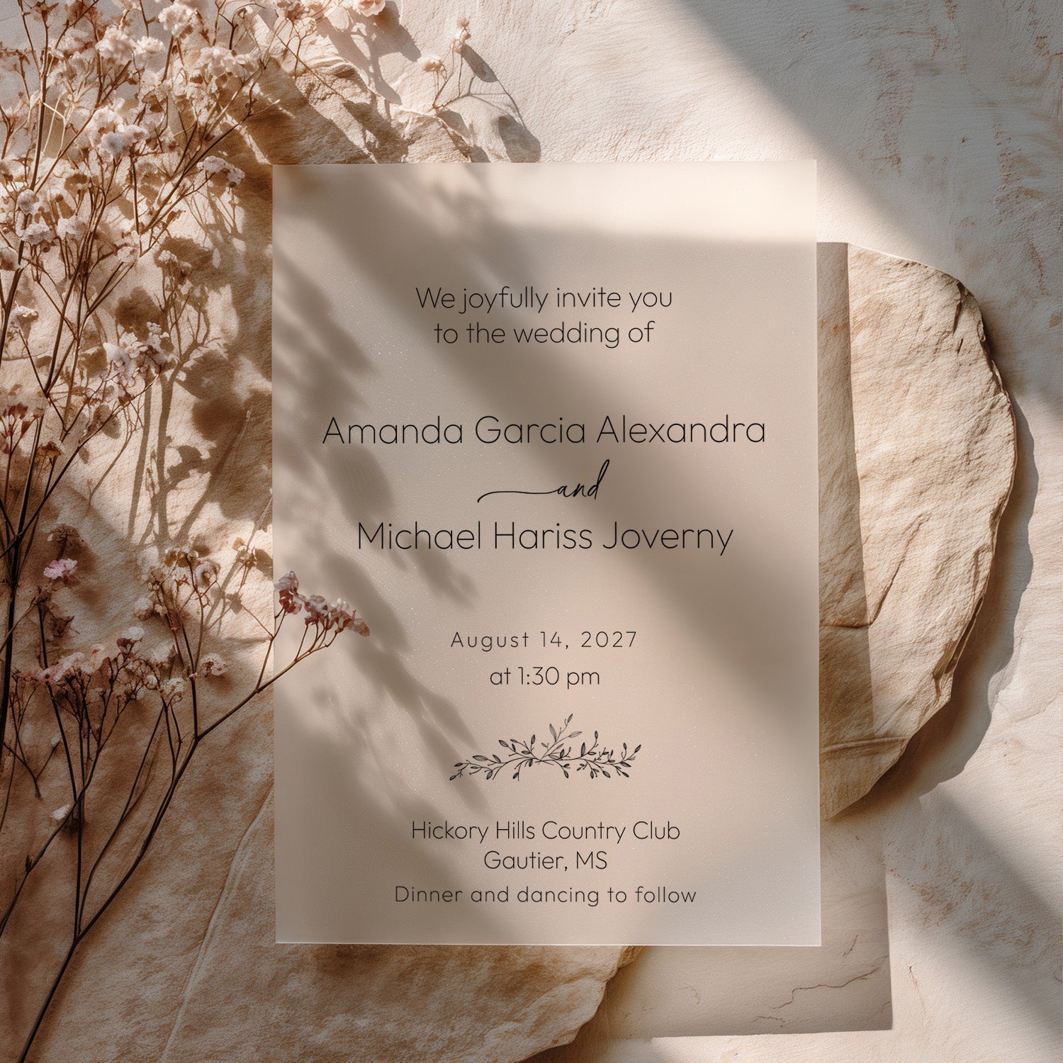 Translucent vellum wedding invitation printed with refined black serif lettering with the couples’ names, arranged with dried blush florals, beige stones, and a minimal natural background. XOXOKristen