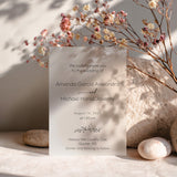 Modern frosted vellum wedding invitation printed with delicate serif and script text with the couples’ names, styled among dried floral stems and smooth neutral beige lighting. XOXOKristen
