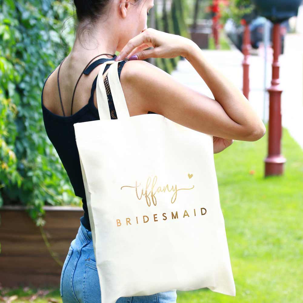 Personalized bridesmaid tote bag with gold foiled lettering and heart accents. Customizable for as maid of honor, flower girl, matron of honor or other custom  wedding roles – XOXOKristen