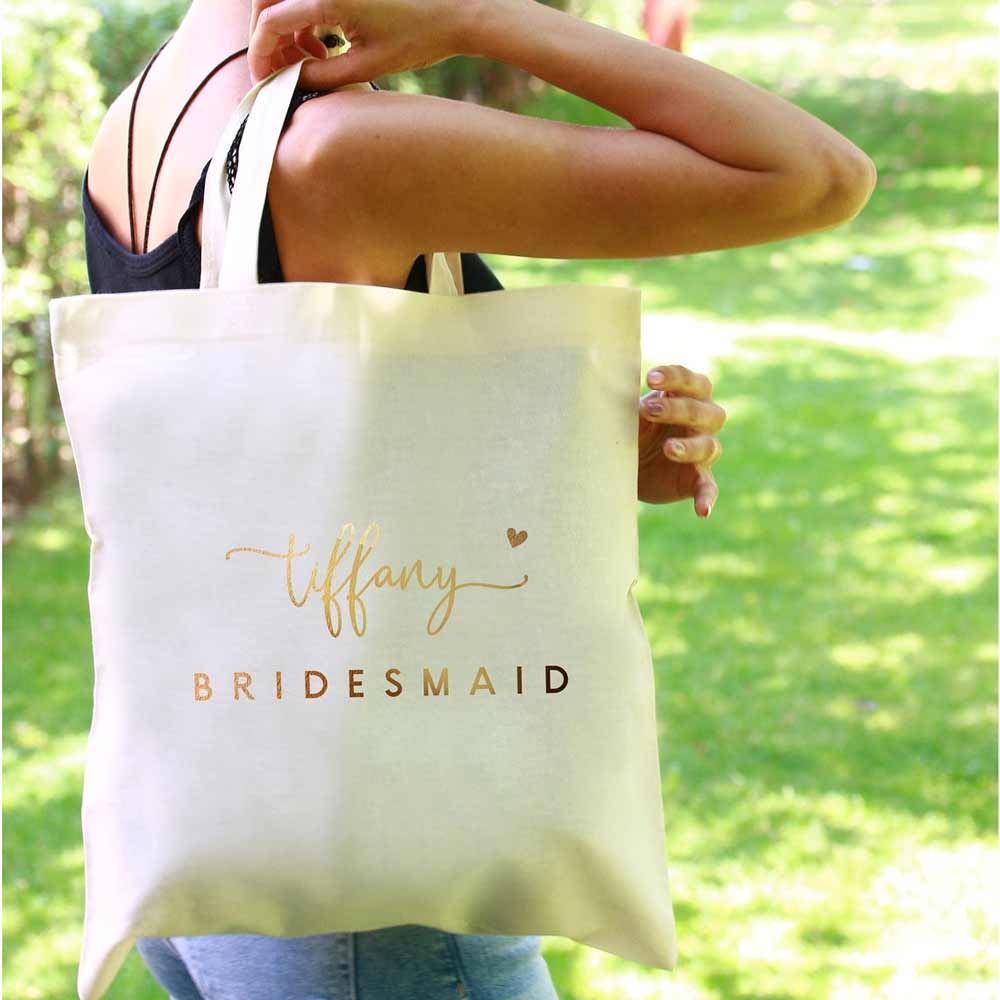 Personalized bridesmaid tote bag with gold foiled lettering and heart accents. Customizable for as maid of honor, flower girl, matron of honor or other custom  wedding roles – XOXOKristen