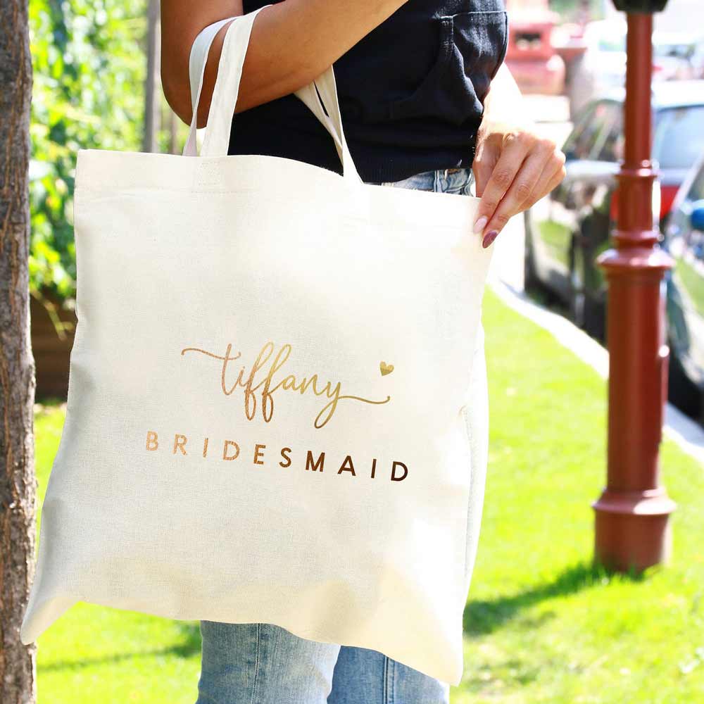 Personalized bridesmaid tote bag with gold foiled lettering and heart accents. Customizable for as maid of honor, flower girl, matron of honor or other custom  wedding roles – XOXOKristen