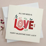 Valentine’s Day card with bold red typography spelling “LOVE”, floral accents, and text “All we need is love”, styled with white envelope — XOXOKristen.